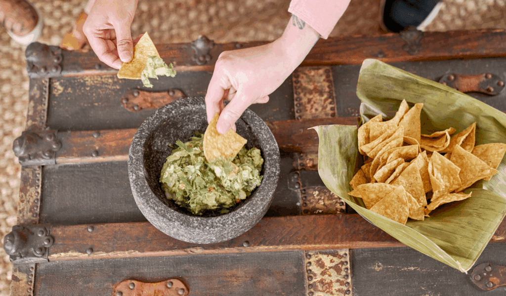 Hand dipping a chip into a bowl of fresh guacamole at La Posada Milford event